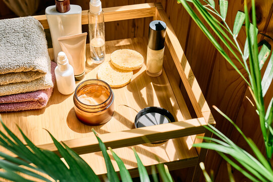 Skincare and beauty products, facial cream, towels and a houseplant arranged on a wooden tray in warm natural sunlight, representing personal care and a daily beauty routine.