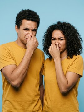 Young African American Couple Pinching Noses and Making Disgusted Faces Due to Bad Smell on Blue Background