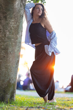 Woman contemplating sunset in a park leaning on a tree