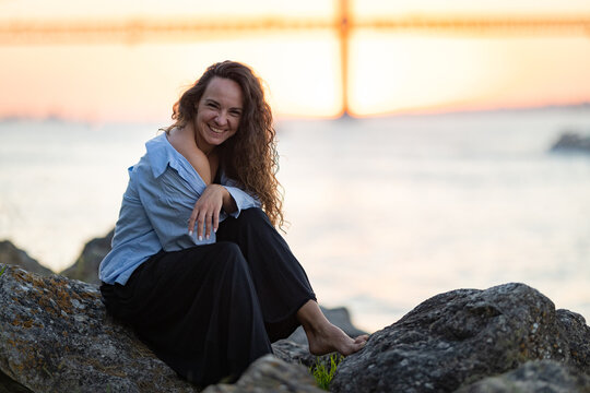 Happy woman relaxing on rocks watching sunset over ocean