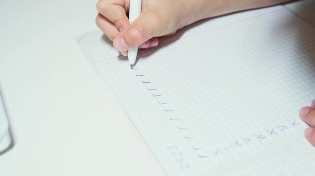 Child traces handwritten English alphabet letters with pen on graph paper during early handwriting practice, following diagonal row of characters to develop writing skills and letter formation