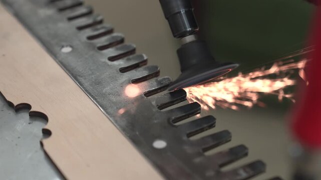 A worker polishes, grinds, and sharpens homemade blades using a handheld pneumatic grinder.