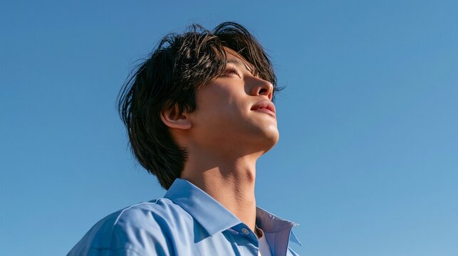 青空の下で静かに上を見上げて物思いに耽るシャツ姿の若い男性の横顔。若者の進路相談、就職転職支援、ライフスタイル特集に最適なポートレート写真（文字入れ用余白・コピースペース付き）