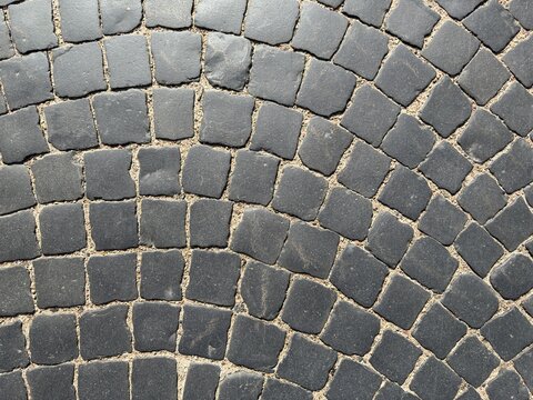 Old cobblestone pavement texture background top view. Ancient basalt stone road surface with dark square blocks and arc pattern for modern urban architecture sidewalk concept.