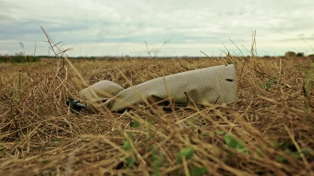 Close-up shot of discarded plastic waste and litter lying among dry grass in a rural field under soft overcast light.