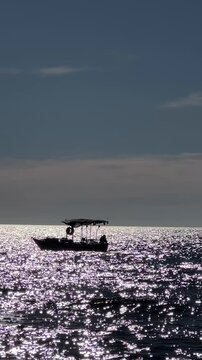 Scenic silhouette of small boat sailing on a glittering sea at twilight shimmering water.