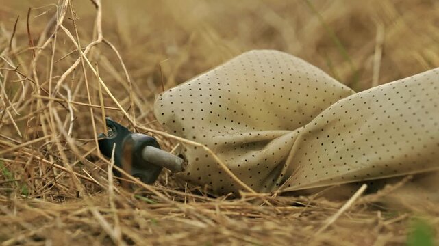 Close-up shot of discarded plastic waste and litter lying among dry grass in a rural field under soft overcast light.