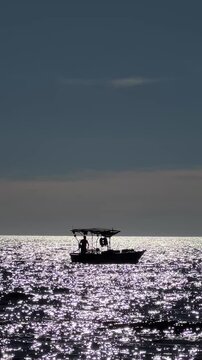 Scenic silhouette of small boat sailing on a glittering sea at twilight shimmering water.