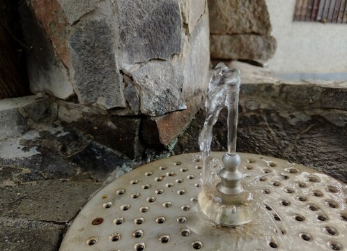 ​Water stream flowing from a public stone drinking fountain outdoors