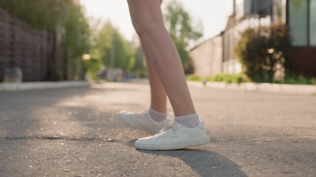 Close up of young woman legs and feet as woman walks down outdoor street. focus remains on movement from mid calf to white sneakers with laces while soft sunlight illuminates her skin