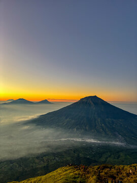 Stunning sunrise view of Mount Sumbing in Central Java, Indonesia, surrounded by misty valleys, rolling hills, and dramatic golden morning light