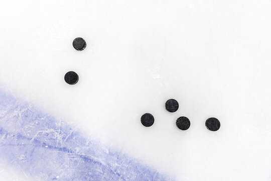 Ice hockey pucks scattered on a scratched ice rink, top view of black pucks on frozen surface with copy space.