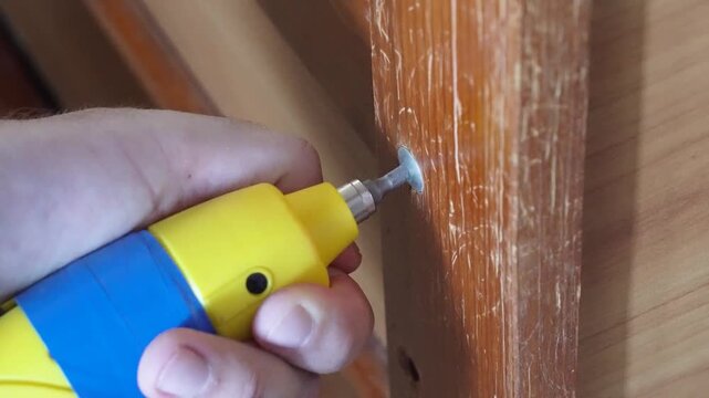 Hand using an electric screwdriver to fasten hardware into wooden furniture during a home repair and DIY project.
