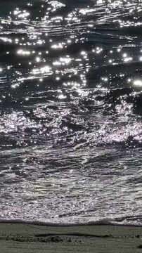 Close up of ocean wave crashing on beach with glittering sun reflections real time.