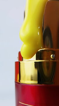 Close up of red product packaging with gold cap and thick yellow liquid flowing over the container. Cosmetic or skincare texture concept.