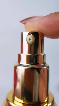 Front close up of a finger pressing a product bottle cap, dispensing a small amount of yellow liquid. Cosmetic or skincare packaging concept.