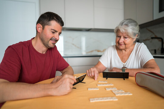 Adult son and senior mother play tile game at home