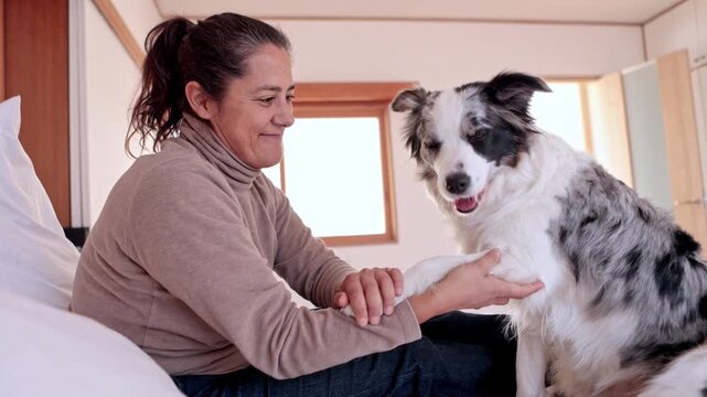 Happy woman petting her cute Border Collie dog on the bed