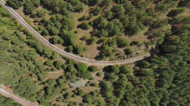 Aerial top view of winding narrow gauge railway curving through green forest in Mokra Gora, Serbia. Small station in mountain, 4k