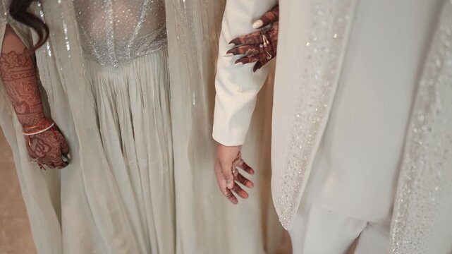 Close-up of newlywed bride and groom in white wedding attire holding hands with bridal mehndi henna