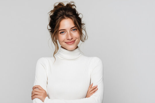 Portrait of a happy, smiling woman in a white turtleneck sweater, standing with her arms crossed and looking at the camera.