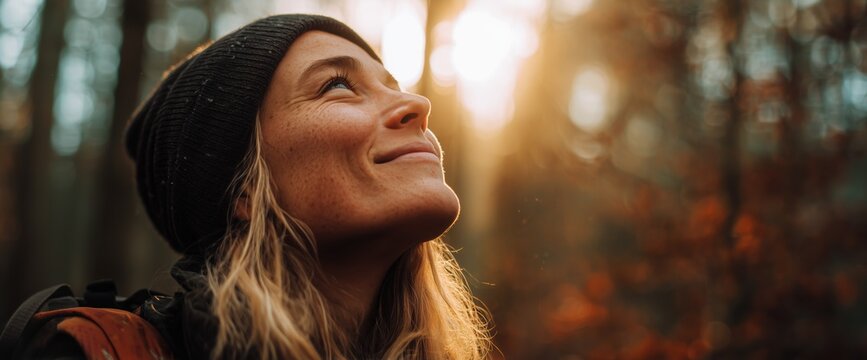 A woman in her late thirties, with blonde hair, hiking, is standing outside at sunrise in the woods.