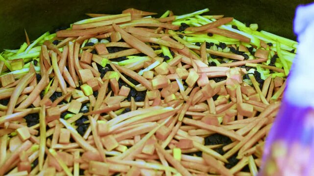 Gloved chef hand leveling sliced carrots, peas and raisins in large metal kazan for Uzbek plov