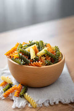 Dry tricolor fusilli pasta in bowl on wooden table