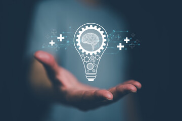 Hand holds digital light bulb with brain and gears, representing creative thinking, innovation, intelligence, problem solving, brainstorming, technology, new ideas and business solutions. © panya7