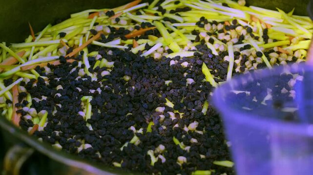 Close-up of chef hand adding raisins to Uzbek plov in large metal cauldron