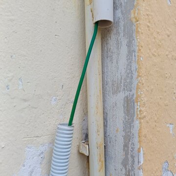 Exposed Green Electrical Wire Hanging from Damaged PVC Conduit Pipe