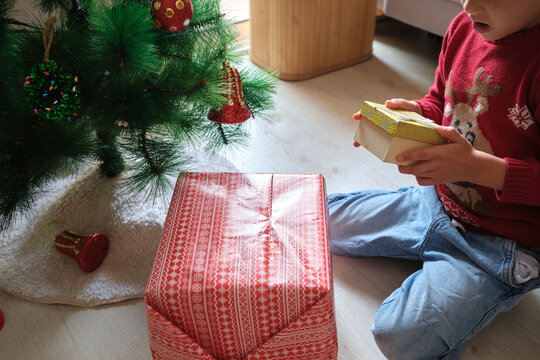 An unrecognisable child opening a Christmas present under a decorated tree