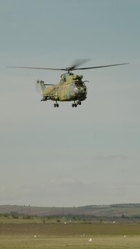 Vertical Screen: A combat helicopter flies in the air during an air show at an airport. People watch as it demonstrates its flying skills in bright weather.