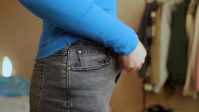 Overweight woman struggling to button tight jeans after postpartum body changes. Concept of weight loss, belly fat, and post pregnancy body positivity.
