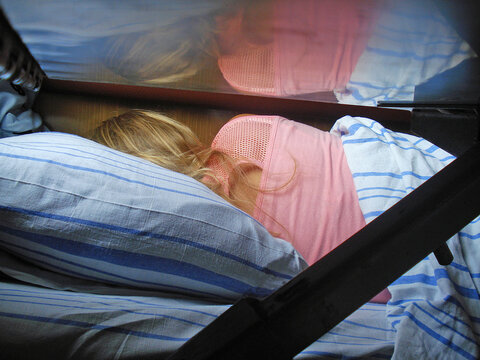 Woman in pink t-shirt sleeping on bunk bed inside passenger train compartment with blue striped pillow.