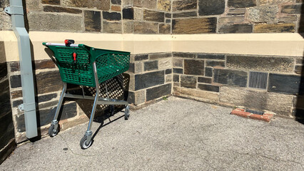 Green plastic shopping cart abandoned beside a textured stone wall, casting shadows on the ground © Chloe