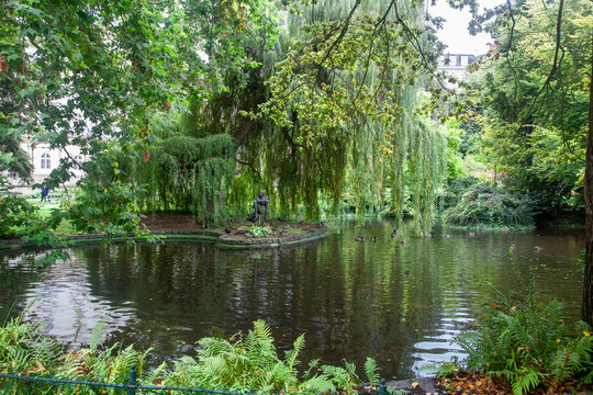 A mermaid sculpture next to a pond under weeping willows
