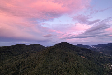 Fototapeta premium Stunning aerial panorama of dramatic pink and purple sunset clouds over dark green mountain ridges