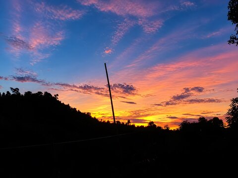 Colorful sunset sky with orange and purple clouds above a dark silhouetted hillside golden hour clouds formations
