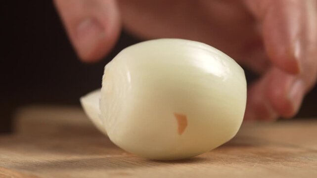 Chef sharp knife cutting peeled whole sweet onion in half on wooden cutting board