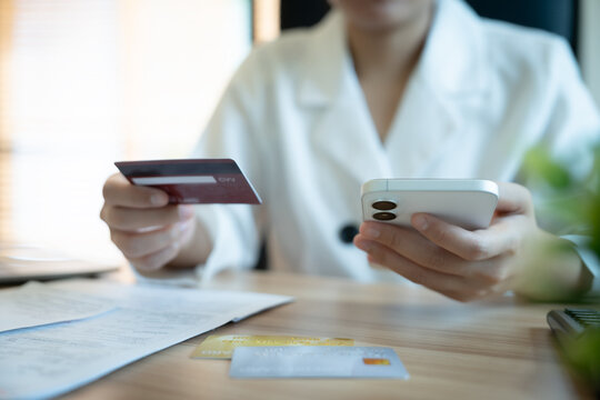 Woman holds phone and credit card at desk. Soft focus highlights her focused, calm demeanor. Natural light bathes the workspace subtly. Perfect for e-commerce, financial services