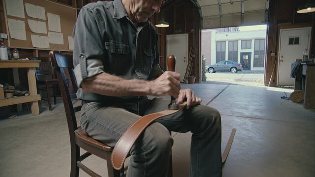 Placing metal stamp, man wearing rolled-sleeves stamping leather strap with mallet