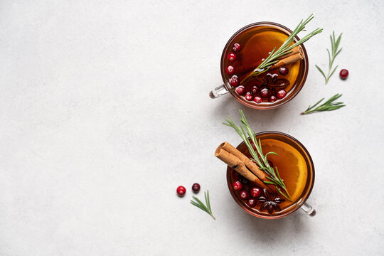 Hot winter drink with orange, cranberries, cinnamon, rosemary and spices in glass mugs, close up Christmas beverage