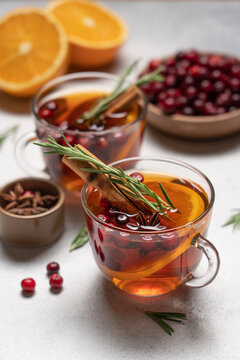 Hot winter drink with orange, cranberries, cinnamon, rosemary and spices in glass mugs, close up Christmas beverage