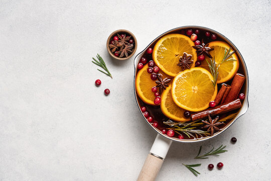 Hot mulled wine with cranberries, orange, rosemary, cinnamon and spices in a pot, Christmas winter drink on a light background with copy space
