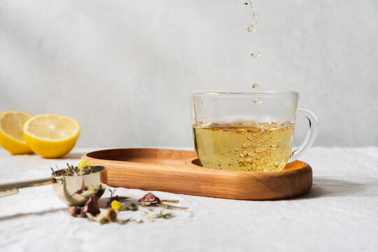 Herbal tea pouring into a transparent glass cup, warm natural beverage on a light background, healthy drink concept