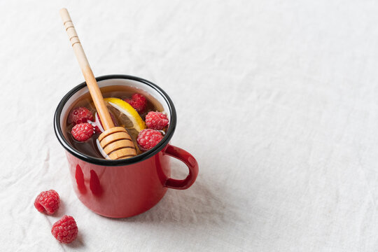 Raspberry tea with lemon and honey served in a red mug on a table, warm homemade beverage for cozy autumn and winter days