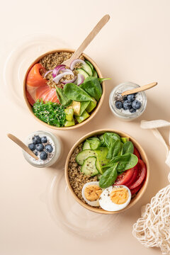 Healthy protein bowls with smoked salmon, egg, quinoa, avocado, spinach, cucumber and chuka seaweed salad in cardboard containers, served with chia seed yogurt and blueberries in glass jars 