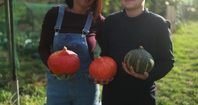 Mother and son holding organic pumpkins at vegetable home garden - Family people having fun during fall season - Autumn lifestyle concept - UGC wide lens content