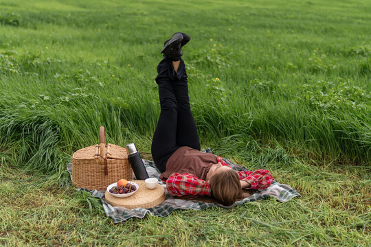 Summer meadow picnic featuring a woman lying on a blanket with legs raised enjoying nature